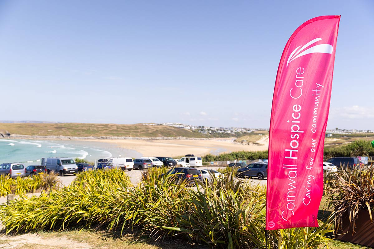 Cornwall-Hospice-Care-Banner-Flag-and-View-1-Bowgie-Inn Cornwall Hospice Care Banner Flag flying at Bowgie Inn with car park and Crantock beach in background